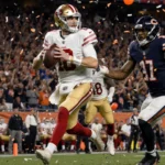 Brock Purdy throws a 49ers pass with Christian McCaffrey sprinting and a packed stadium crowd in the background