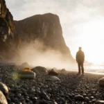 Lone curler standing with curling stone and mist swirling around feet on granite coast at dawn