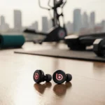 Black Beats Powerbeats Fit earbuds resting on a wooden floor with a gym setting and a blurred cityscape behind for workout.