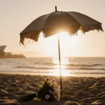 Umbrella standing beside abandoned bouquet with sunset casting warm light on sand