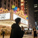 Bowen Yang holding mic with marquee reading The End in front of Rockefeller Center and festive lights