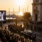 Funeral procession moving along waterfront promenade with golden sunset lighting Notre-Dame-de-l