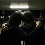 Students huddling on Brown quad with fluorescent lights and a guard in distance one hand on another’s shoulder