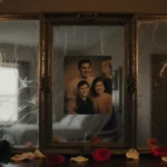 Family portrait frame hanging on dim wall with candlelight glow and scattered rose petals