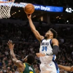 Cooper Flagg soars with ball and three-pointer over defenders with packed crowd and scoreboard reading 42-40