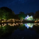 Lake reflects illuminated trees at Dallas Arboretum with starry winter evening sky and lantern-lit pathways