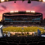 Dallas Cowboys stadium illuminated at night with pink-orange sky and golden field surrounded by trophies