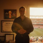 David Balyeat stands proudly in front of a 1994 FIFA World Cup program with Cotton Bowl stadium visible behind