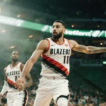 Deni Avdija drives to the basketball basket with arm outstretched passing as Klay Thompson watches behind him in a scene.