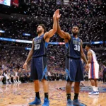 Cooper Flagg and Anthony Davis highfiving with arms raised in triumph amid confetti cheering fans at Mavericks overtime win.