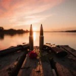 Broken shotgun shells lie side by side on a weathered dock with a single rose petal blooming nearby beneath a Florida sunset.