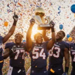 Gordon high school football team celebrates championship victory holding trophies with sunset glow and confetti in stadium.