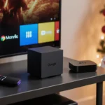 Google TV Streamer sits on a TV stand surrounded by Roku Chromecast and Apple TV with lighting and a holiday tablecloth behin