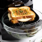 Grilled cheese sandwich emerging from air fryer basket with golden crust and melted mozzarella and fresh herbs