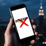 Hand holding smartphone with Amazon logo and red X and blurred night cityscape in background and cyber threat