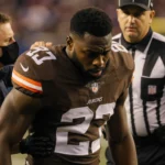 Browns rookie Quinshon Judkins being lifted off the field by medical staff with referee nearby on Buffalo Bills turf