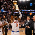 Knicks center lifts NBA championship trophy with confetti swirling and coach Fizdale applauding behind him