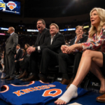 Martha Stewart sits courtside watching a basketball game with arena lights and a Jalen Brunson jersey with gauze bandage.