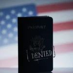 Folded US passport shows a denied stamp with a blurred American flag in blue‑gray background
