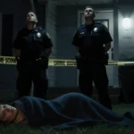 Two police officers standing behind crime scene tape looking up at sky with a woman lying on floor under emergency light glow