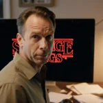 Randy Havens smiles at camera with computer screen showing a Stranger Things screenshot and dimly lit room