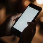 Person holding a smartphone with a clean screen showing a subtle grid and a dimly lit warm background.