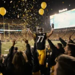 Steelers fans cheer with arms raised under golden lighting with confetti falling.