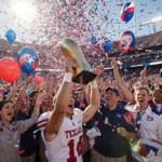 Victorious player raises trophy aloft with cheering fans in red and blue confetti swirling and banners flashing