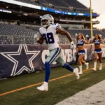 Trevon Diggs sprinting down Cowboys sideline with AT&T Stadium turf and sunset glow behind cheering cheerleaders
