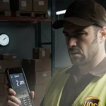 UPS worker checks clocking‑in screen with tired face and dim warehouse backdrop