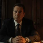 Alan Jackson sits at desk with legal papers and glowing lamp showing concern on his face