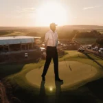 Jack Nicklaus silhouette standing on golf course green with half-built event center and sunset lighting the construction site