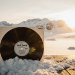 Vinyl record lying on wooden table partially buried in snow with golden Arctic sunset glow and gentle breeze on a quiet snowy
