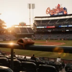 A baseball glove sits on a dugout rail with a worn ball and sunset light over a stadium featuring the Orioles logo