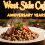 Steaming black-eyed peas with crispy bacon sit on a table with parsley garnish near a West Side Cafe menu board and New Year