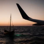 Silhouette of a Boeing 777 wing floats over dark southern Indian Ocean with bioluminescent waves and a wooden boat drifting.