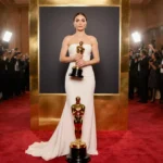 Brazilian actress holding Golden Globe trophy with cheering crowds and camera flashes behind her