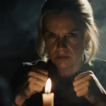 Rhea Seehorn sits with clenched fists and narrowed eyes lit by a flickering candle in a smoky room
