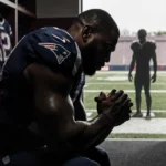Barmore bends head with hands clasped in dim locker room with football gear and faint shadow of Diggs behind