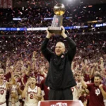 Indiana coach Curt Cignetti holds championship trophy high with red and cream fans cheering and confetti swirling