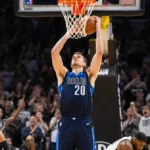 Cooper Flagg shooting three-pointer with Mavericks logo overhead and bench celebrating behind