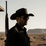 Cowboy in hat and sunglasses stands at shooting range with rifle leaning against target stand and Texas backdrop