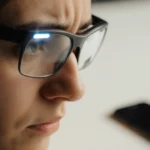 Person wearing smart glasses with flashing light looks disappointed while abandoned smartphone sits on table