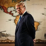 Donald Trump standing with hands behind and gaze toward the camera and South America map featuring Venezuela military hints