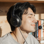 Person sitting on desk with earbuds on face and plant nearby enjoying music in warm lighting