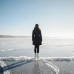Figure skater standing at frozen lake edge with blades etched into ice and gradient sky transitioning to deep indigo