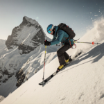 Skier ascending a snowy mountain slope with a pole planted and route marker held toward the icy peak in golden light