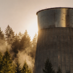 Cooling tower glints with sunset light as misty forest rises behind