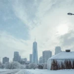 Streetlamp illuminates winter cityscape with snow-covered rooftops and falling snowflakes