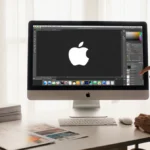 Hand opens creative app suite on iMac with Apple logo glowing and design boards nearby